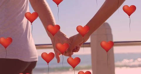 Multiple heart balloons floating against mid section of couple holding hands at Fotos Stock
