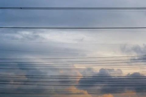 Multiple horizontal high voltage cable lines across stormy clouds, at sunset. Stock Photos
