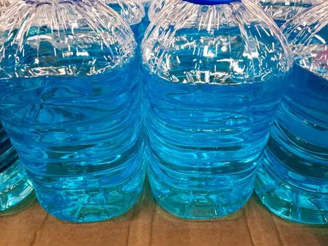 Multiple large plastic bottles lined up with bright blue liquid, possibly a.. Fotos de archivo