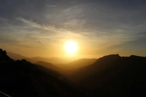 Multiple layer of mountain fading over a veiled sun Stock Photos
