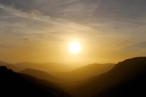 Multiple layer of mountain fading over a veiled sun Stock Photos