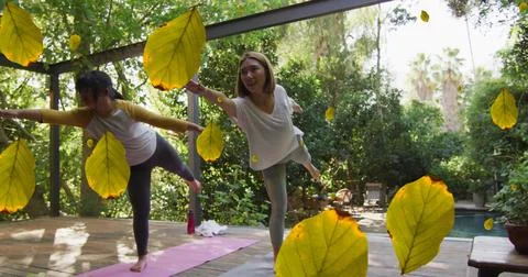 Multiple leaves icon falling against two asian women performing yoga Stock Photos