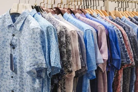 Multiple men's short-sleeved button-up shirts hang on wooden hangers. They di Stock Photos