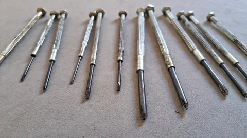 Multiple metal precision screwdrivers arranged neatly on a grey surface Stock Photos
