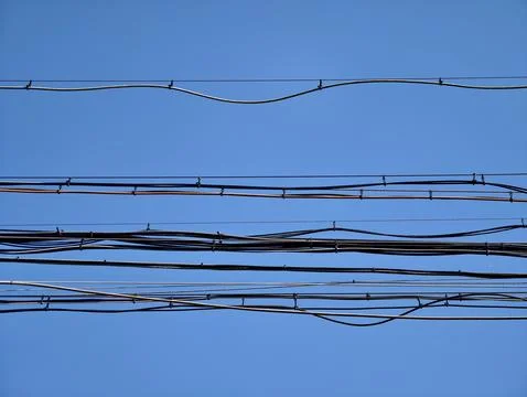 Multiple overhead utility cables crossing clear blue sky, with curved insul.. Stock Photos