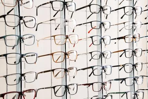 Multiple pairs of eyeglasses displayed on a white rack for sale at an optic.. Stock Photos