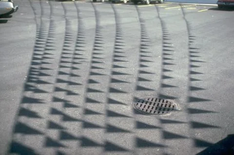 Multiple pennant shadows casting a pattern on pavement of parking lot w. drain i Foto stock