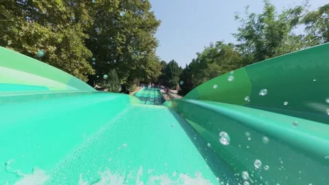Multiple people racing down a wide, green multi-lane water slide on a sunny day Video stock 316398771
