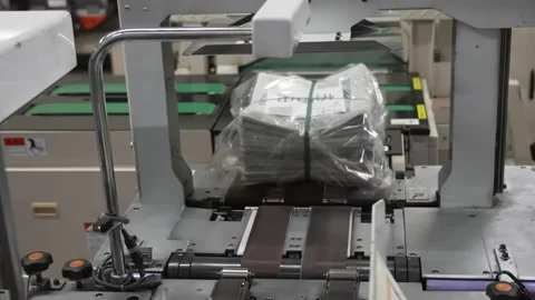 Multiple plastic-wrapped newspaper bundles moving along automated conveyor Stock Footage 337890130