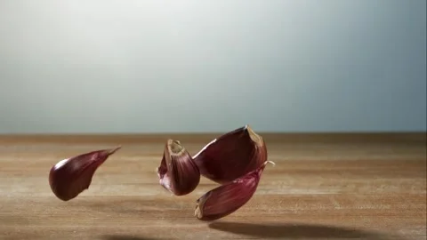 Multiple Red Garlic Cloves Falling And Bouncing On A Light Brown Wooden Stock Footage 326290650