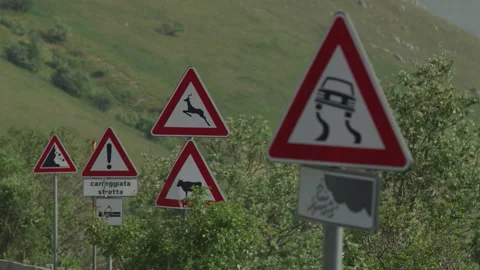 Multiple Road Warning Signs on Curving Mountain Route with Green Hills Stock Footage 338018789