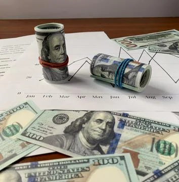Multiple rolls of currency are secured with rubber bands, surrounded by Stock Photos