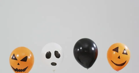 Multiple scary faces printed halloween balloons floating against grey background Stock Footage 163450630