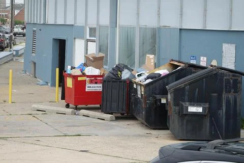 Multiple small dumpsters full of trash by the side of a building Stock Photos