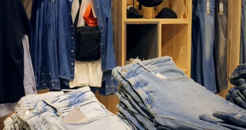 Multiple stacks of folded blue jeans sit on a wooden display table in a clothing Stock Footage 314466145