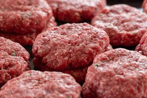 Multiple stacks of freshly processed raw hamburger patties on display in meat Stock Photos