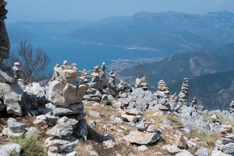 Multiple stone cairns stand on a rocky summit overlooking a deep blue bay Stock Photos