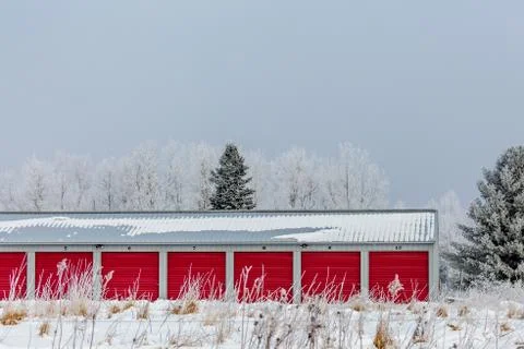Multiple storage units with red doors next to woods in the winter Stock Photos