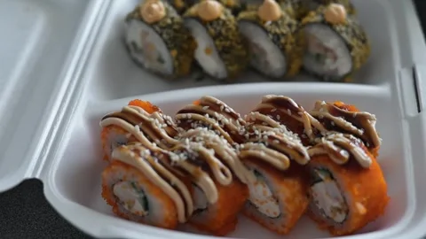 Multiple sushi rolls are arranged neatly in takeout containers. The footage Stockbeeldmateriaal 337556311
