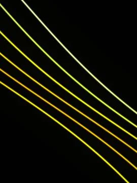 Multiple thin yellow, lime, and green lines angle across a black background.. Stock Illustration