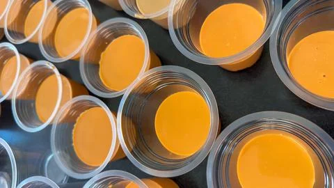 Multiple transparent glass cups filled with vibrant orange juice arranged Stock Photos
