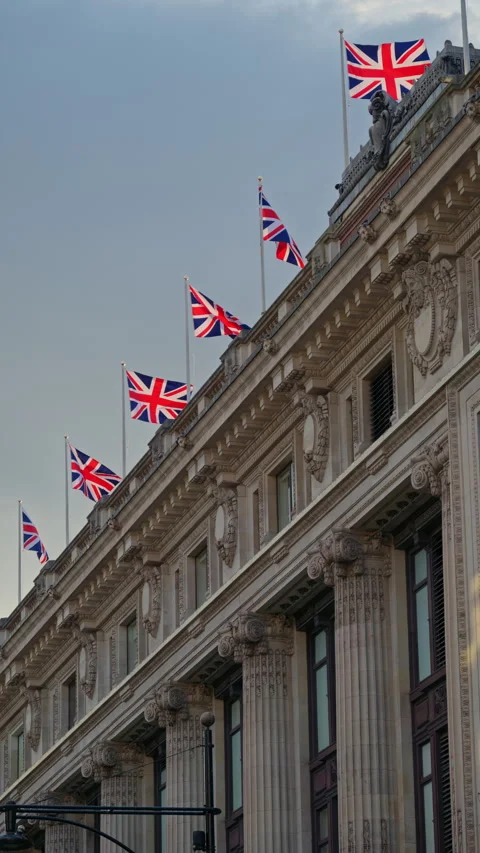 Multiple Union Jack flags waving atop a classic London building under a cloudy 스톡 동영상 315542436