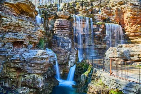 Multiple waterfalls pouring over cliffs into river by paved path Stock Photos