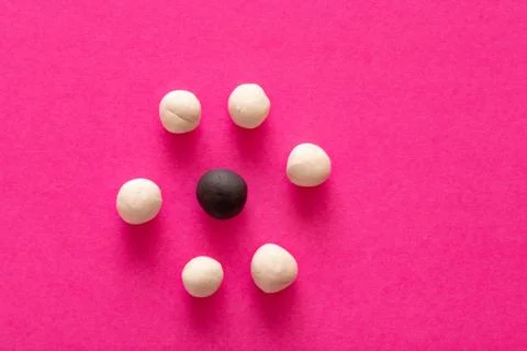 Multiple white balls surrounding a single black one on pink vibrant backgroun Stock Photos