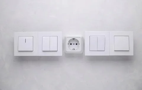 Multiple white electrical switches and socket on wall Stock Photos