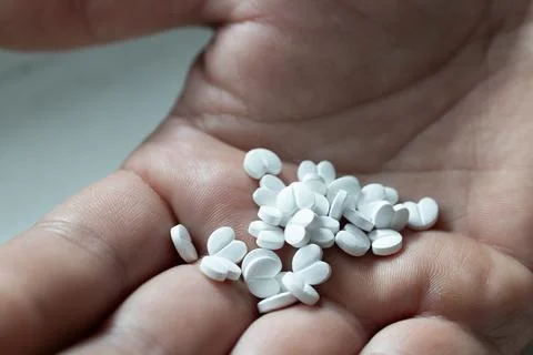 Multiple White Pills Scattered in a Hand Signaling Possible Medication or Stock Photos
