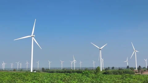 Multiple wind turbines rotate above green farmland under a bright blue sky Video stock 314817298