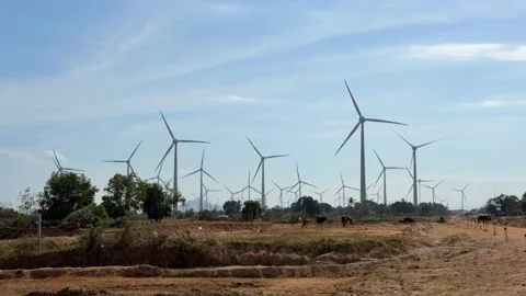Multiple wind turbines rotate steadily across open land, their blades turning Stock Footage 329988562