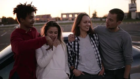 Multiraced happy two couples are leaning on the silver car on the parking. Two Stock Footage 98349243