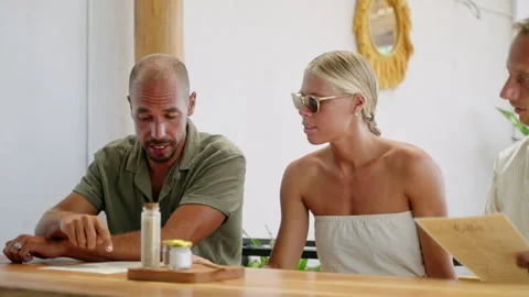Multiracial cheerful friends looking at menu, choosing food in tropical cafe Stock Footage 274752273
