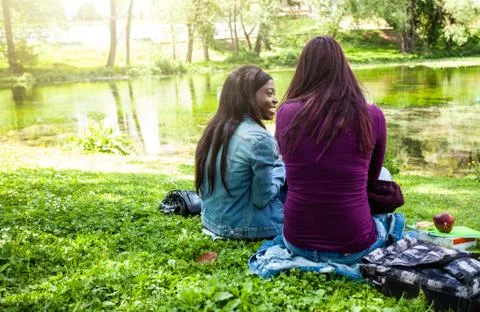 Multiracial couple from behind using laptop and cell phone at the park. Stock Photos