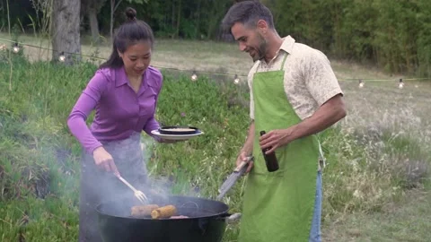 Multiracial couple making barbecue. Smiling middle-aged people cooking outdoors. Stock-Footage 211498150