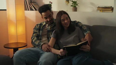 Multiracial couple sitting on the couch and reading book. Stock Footage 302065828