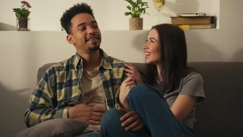 Multiracial couple sitting on couch holding hands and laughing. Stock Footage 302066525