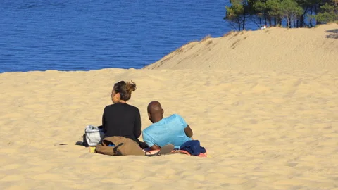 Multiracial couple sitting on the sand of the Dune of Pilat on the Arcachon Bay Stock Footage 176403254