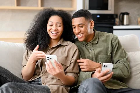 Multiracial couple with smartphone on the couch spending leisure time in social Foto stock