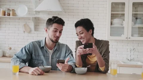 Multiracial couple using mobile phone together at home kitchen. Concept of Stock Footage 238917188