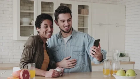 Multiracial couple using smartfon for video call while sitting at the table in Stock Footage 238916614