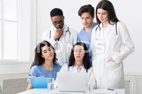 Multiracial doctors looking at laptop, working together in clinic Stock Photos