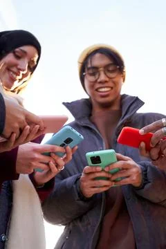 Multiracial friends standing in circle using phone outdoors. Stock Photos