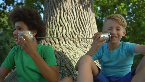 Multiracial friends talking through cans sitting in park, happy childhood, fun Vidéo 117204563