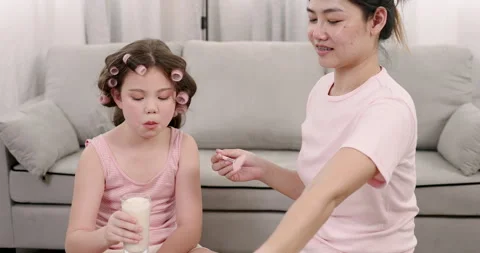 Multiracial girl drinking milk while asian single mother gently combing hair Stock Footage 314277000