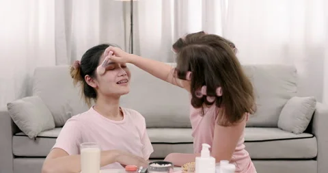 Multiracial girl smiling while softly brushing powder on asian single mother's Stock Footage 327694005