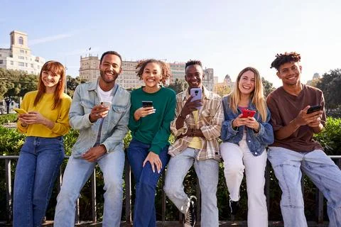 Multiracial group of friends using mobile phone and looking at camera smiling. Stock Photos