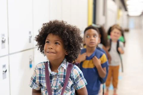 Multiracial innocent elementary school children standing in row by lockers Stock Photos