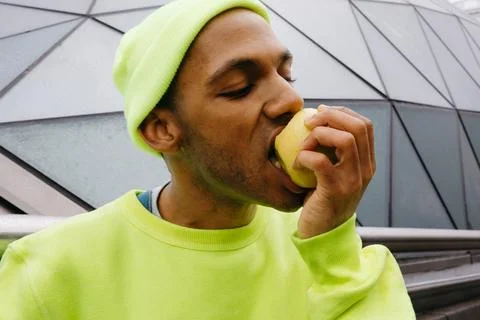 Multiracial man biting apple with satisfaction outdoors Stock Photos